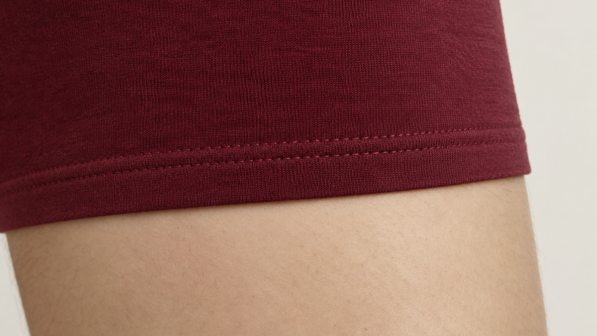 The bound hem of a maroon cotton trunk resting flat against the thigh, showing the stitch line.